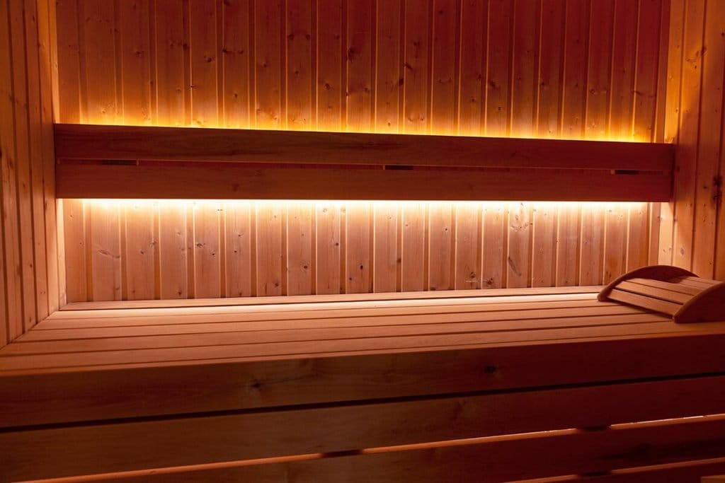 IMG_2894 - LedStore Viihtyisä saunan sisustus puisilla lauteilla ja rauhoittavalla LED-ympäristövalolla, joka korostaa niskatuen rentoutumiseen rauhallisessa ilmapiirissä.