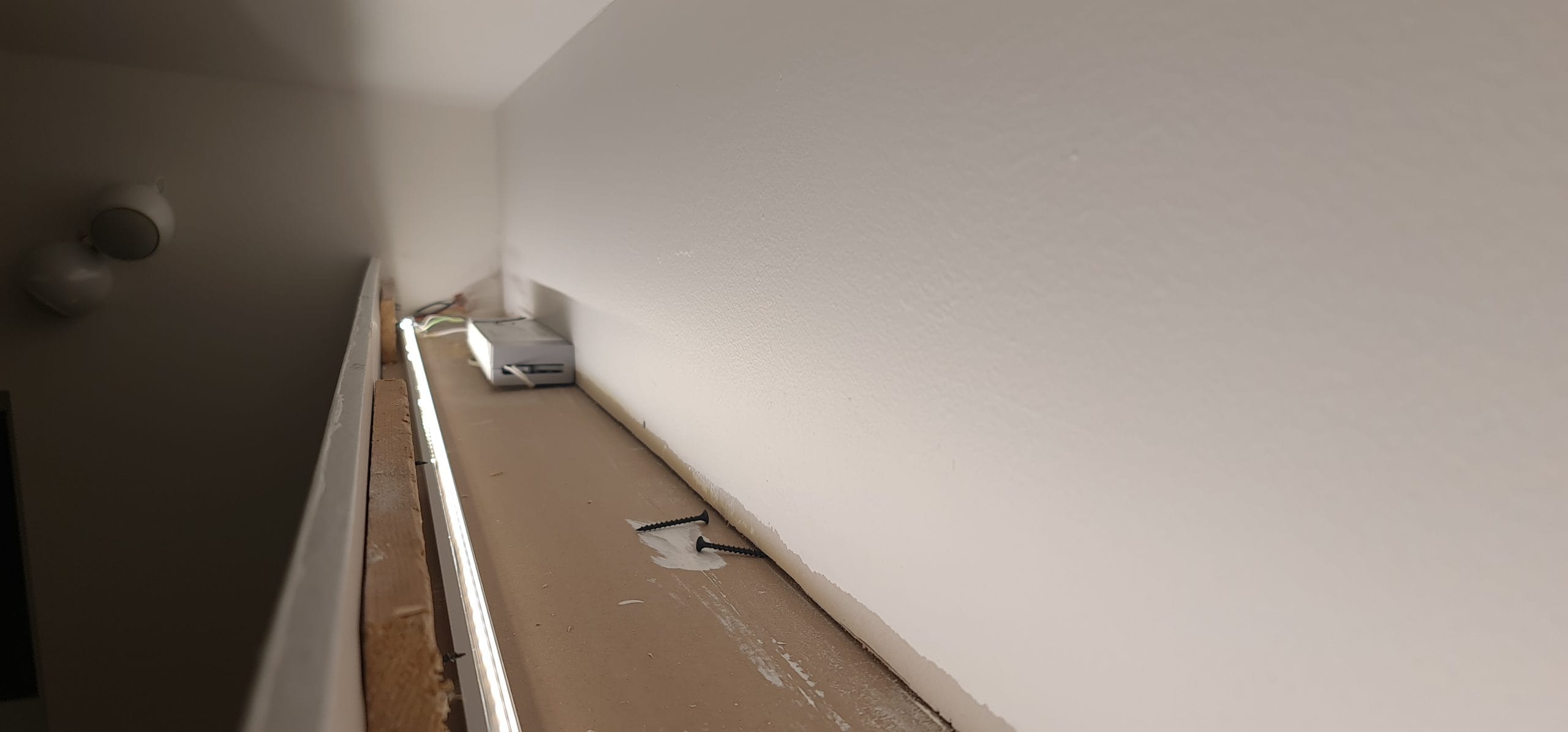 - LedStore Lähikuva kapeasta upotetusta hyllystä, jonka reunaa rajaavat LED-valot, jotka korostavat minimalistista ilmettä valkoisilla seinillä ja pienellä päädyllä.