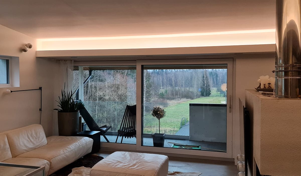 - LedStore Moderni olohuone, jossa suuret lasiovet, kermanvärinen sohva ja kattoon upotettu LED-valaistus, josta on näkymät parvekkeelle ja nurmikentällä.