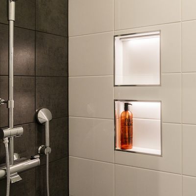 LED-upplyst dusch med vägg i blandat kakel, inbyggd hylla med spotlight och brun tvålpump.
