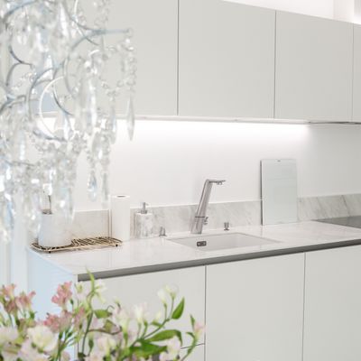 Minimalistiskt vitt kök med bänkskivor i marmor, modern kran och kristallkrona som framhäver LED-belysningen.