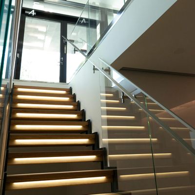 Trapphusbelysning lyser upp glastrappor; moderna LED-lampor förbättrar atmosfären i interiören, med naturligt ljus ovanför.