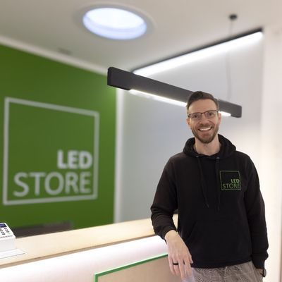 En man i LED STORE-huvtröja vid belysningsdisk, grön LED-skylt, modern butiksmiljö