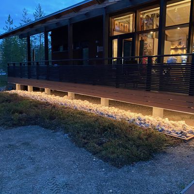 En modern träbyggnad med en LED-upplyst veranda bland stenar, skymningshimlar och träd - för mer kvällsstämning och energieffektivitet.