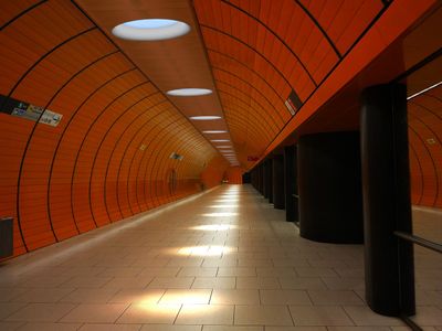 Tom, väl upplyst orange tunnelbanestation med klinkergolv, svarta pelare, böjd tunneldesign och väggskyltar