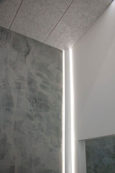 Modern hörninredning med texturerade grå väggar och vertikala LED-lampor; minimalistisk och ljus.