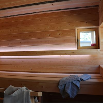 LED-belyst bastuinteriör i trä med bänkar, litet fönster och handdukar; perfekt belysning för en avkopplande spaupplevelse.