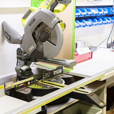 Alternativ text: en Ryobi kap- och geringssåg på en arbetsbänk omgiven av organiserade hyllor med små blå lådor och olika verktyg i en väl upplyst LED-belysningslösning.