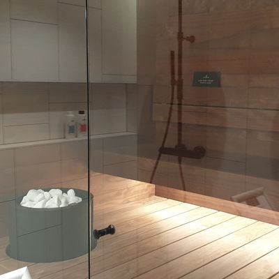 Modernt basturum med träväggar, glasdörr, stenhink, duschhuvud; perfekt atmosfär med LED-belysning för avkoppling och komfort.