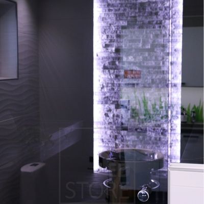 Modernt badrum med strukturerat kakel, bakgrundsbelyst vägg, cirkulärt handfat och spegelbelyst kakel. Elegant LED-belysning framhäver den lyxiga designen.