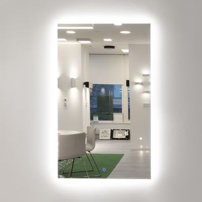 En belyst spegel som speglar en modern inredning med pendellampor, eleganta stolar och naturligt ljus.