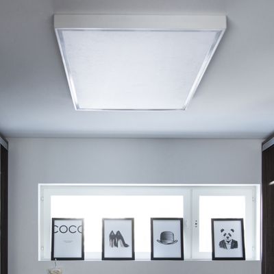 LED-takarmatur som belyser monokroma inramade bilder av text, skor, hatt och panda på en hylla bredvid ett fönster i en modern heminredning.