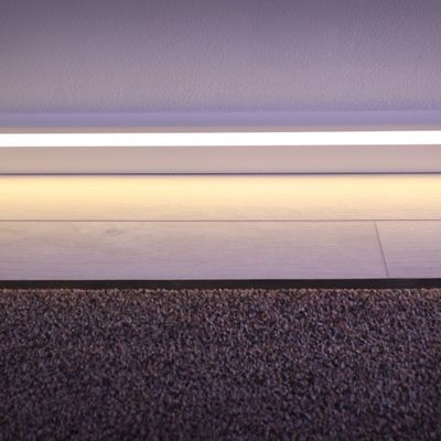 Ett modernt LED-ljusband belyser övergången mellan matta och trägolv och framhäver de vita sockeldetaljerna.