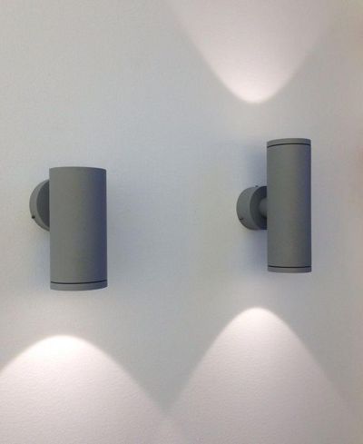 Moderna cylindriska LED-vägglampor kastar mjukt ljus upp och ner på en vit vägg och skapar en elegant atmosfär i en modern ljusdesign.