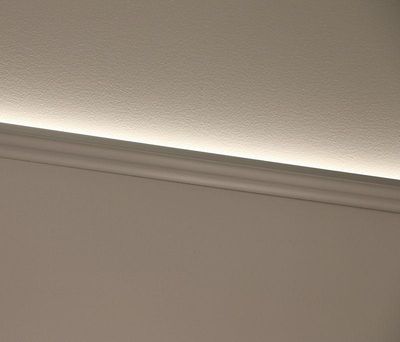 En modern vit golvlist med en subtil LED-ljuseffekt ovanför som lyser upp väggen och framhäver en ren och modern design.