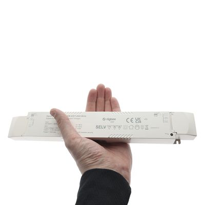Närbild av en hand som håller i en rektangulär Zigbee LED-kontroller med flera tryckta certifikat och symboler för kvalitetssäkring.