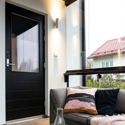 Modernt uterum med energieffektiv LED-belysning, svart dörr, grå soffa med färgglada kuddar, glasväggar som visar upp huset med ett livfullt rött tak.