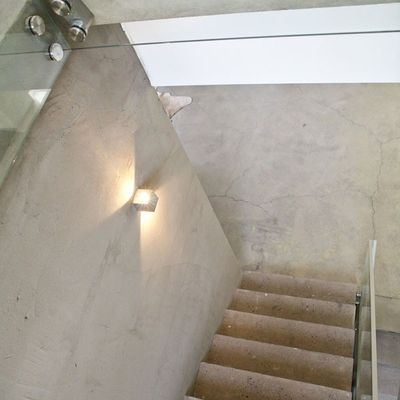 En modern trappa med trappsteg i betong, glasräcke och väggmonterad LED-lampa med varmt sken; den minimalistiska designen bidrar till stämningen.