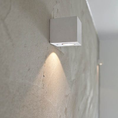 En minimalistisk väggmonterad fyrkantig LED-armatur som skapar ett varmt sken på en texturerad grå vägg för modern interiörbelysning.