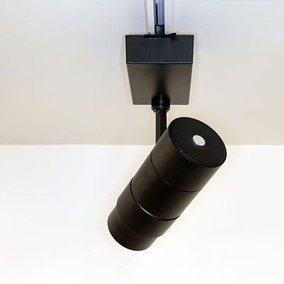 Modern svart cylindrisk LED-armatur för vitt tak, monterad på ett elegant svart skensystem för mångsidiga belysningslösningar.
