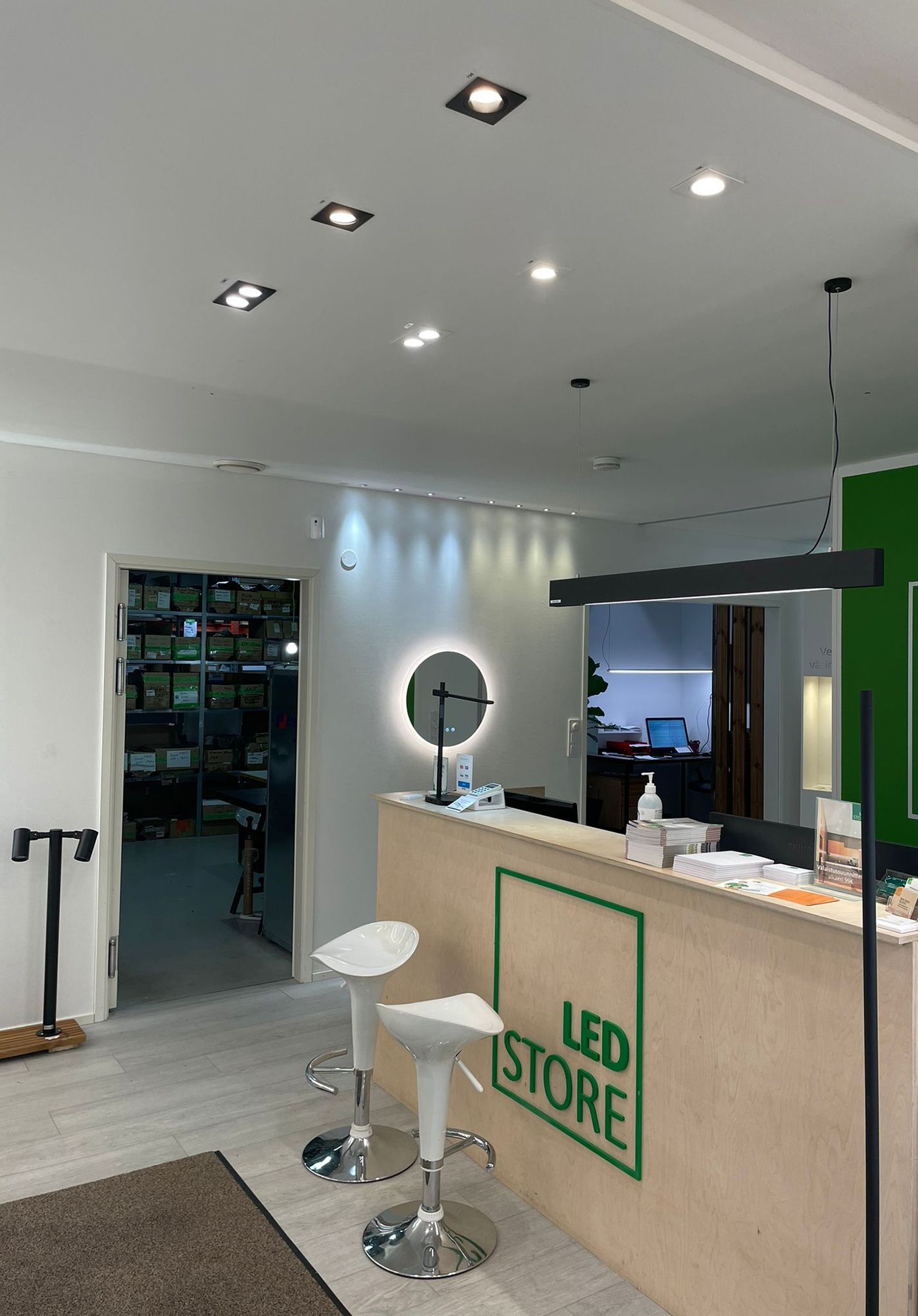 Led-lampor i Ledstores showroom. Spots i taket framför disken och en VIIVA taklampa ovanför disken. Väggen accentueras av 3W spotlights, fasta och riktbara. Moon 600 ljusspegel under spotarna. Ledstore.fi