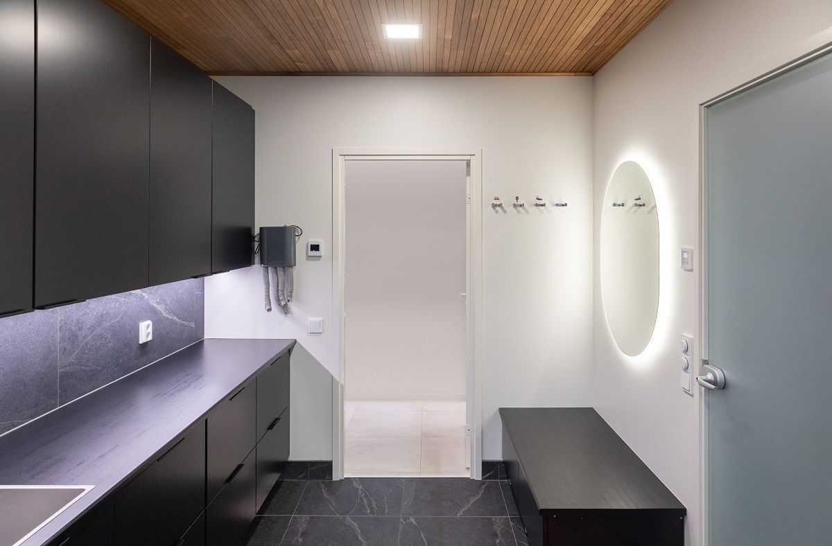 I taket i ett hemvårdsrum lyser en liten rektangulär panellampa, en oval spegel och en LED-remsa upp bänkskivan.