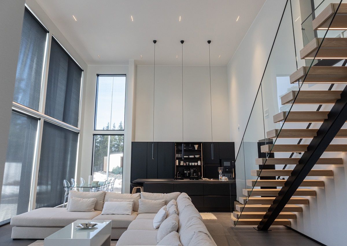 LINJA10 strålkastare för allmänbelysning i det höga taket i vardagsrummet, köket och matplatsen samt tre LED PIIPPU 2.0 pendellampor ovanför köksön. LED-list på trappstegen.