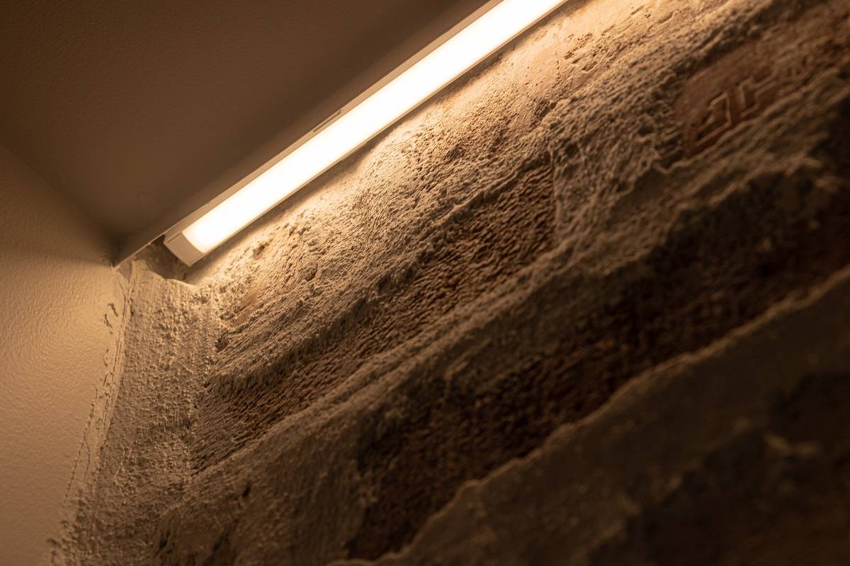 Närbild på installationen av LED-remsan på en accentvägg. LED-remsan är monterad i en ytmonterad aluminiumprofil mellan listen och väggen.