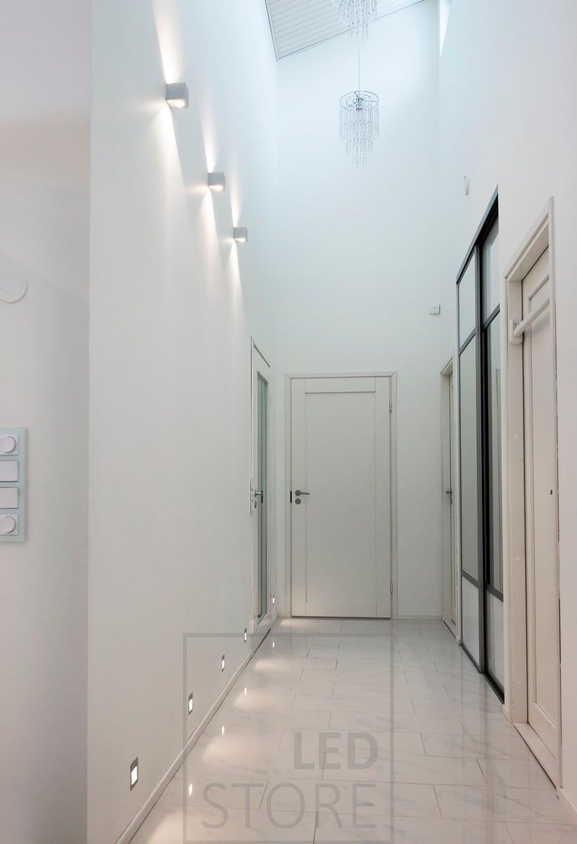 IN-WALL infällda LED-väggarmaturer skapar indirekt ljus i korridoren på golvnivå. Ovanför dem sitter CUBIC led-väggarmaturer som lyser i två riktningar och framhäver rummets höjd. Ledstore.fi