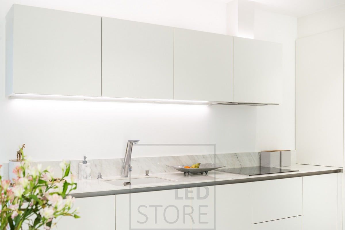 LED-lister som belyser skåpens ovansida och bänkskivan. Det neutrala ljuset framhäver de rena tonerna i det vita köket. Ledstore.fi