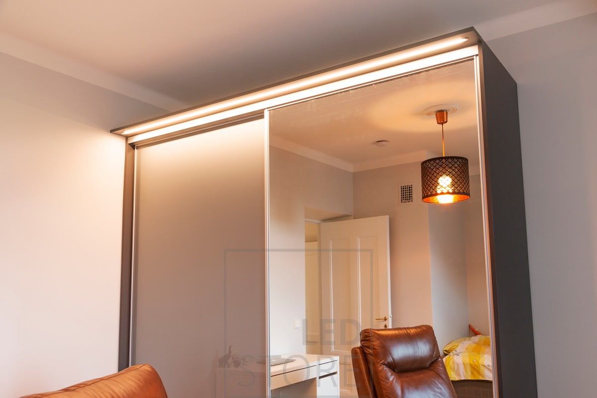 Led-ljusband i en smal infälld profil i en låda som byggts ovanpå ett skåp. Ljuset lyser upp såväl hallen som skåpet och dess innehåll. Ledstore.fi