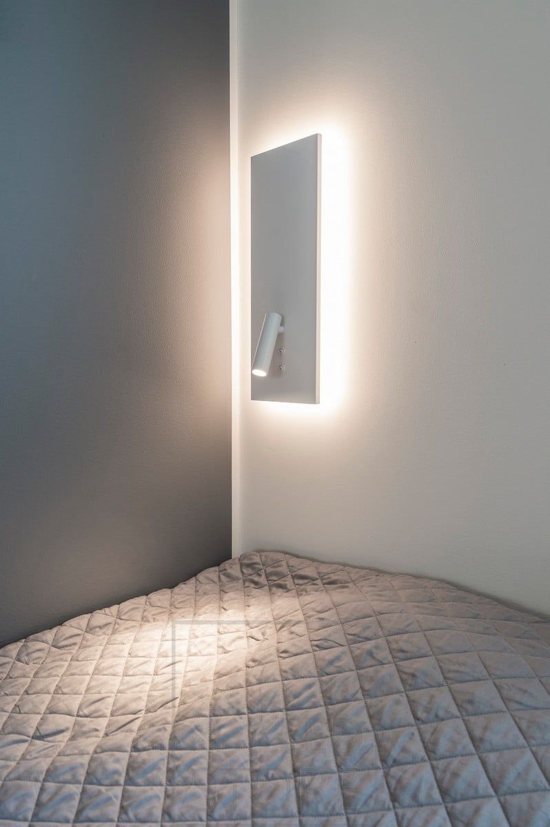 Vägglampa NIGHT i vitt. Med indirekt och mjuk stämningsbelysning i bakgrunden och ett riktat läsljus som tänds med en separat strömbrytare. Ledstore.fi