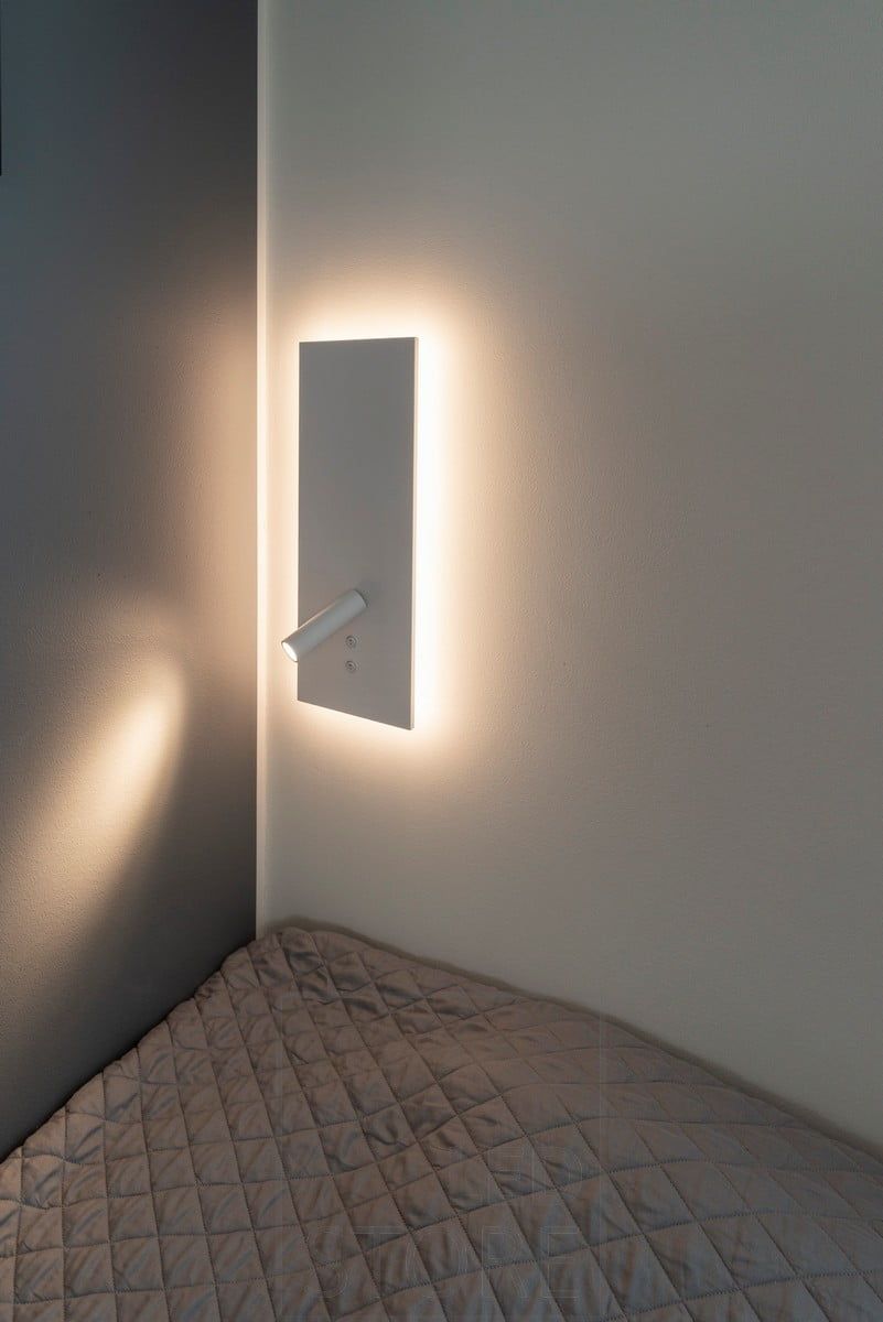 Vägglampa NIGHT i vitt. Med indirekt omgivningsljus i bakgrunden och ett riktat läsljus som tänds med en separat strömbrytare. Ledstore.fi