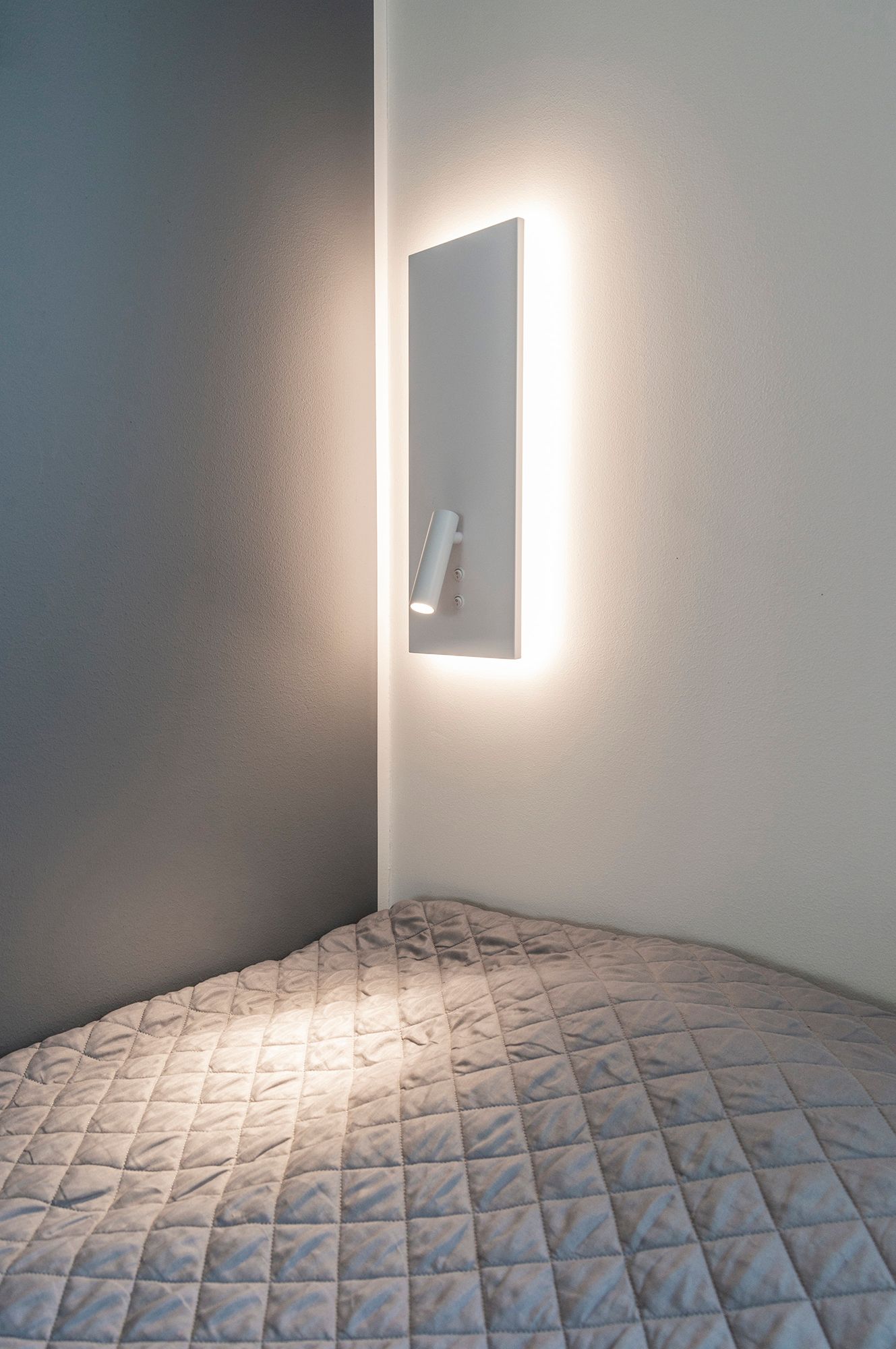 Vägglampa NIGHT i vitt. Med indirekt och mjuk stämningsbelysning i bakgrunden och ett riktat läsljus som tänds med en separat strömbrytare. Ledstore.fi