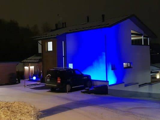 Fasaden på ett modernt hus speglas i det blå ljuset, med ett tunt snötäcke på marken och en bil framför huset.