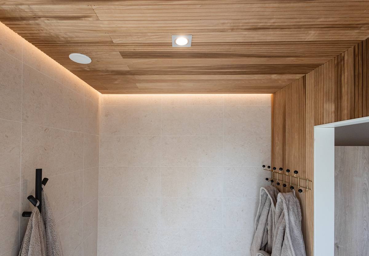 LedStore.fi erbjuder en lösning för det moderna badrummet med modern LED-belysning. De beige kaklade väggarna, trätaket och den infällda LED-belysningen skapar ett fräscht och modernt utseende. Mjuka grå handdukar upphängda på svarta krokar harmoniserar den minimalistiska inredningen.  