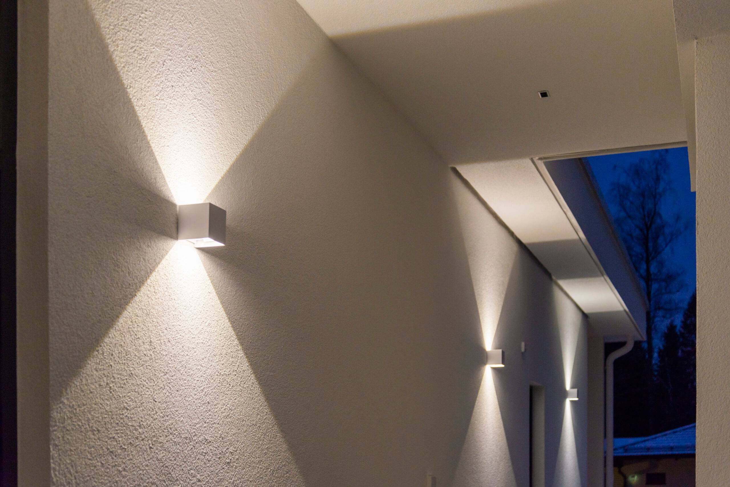 De kubiska vita LED-vägglamporna lyser både uppåt och nedåt, vilket skapar ett skarpt ljusmönster på väggen.