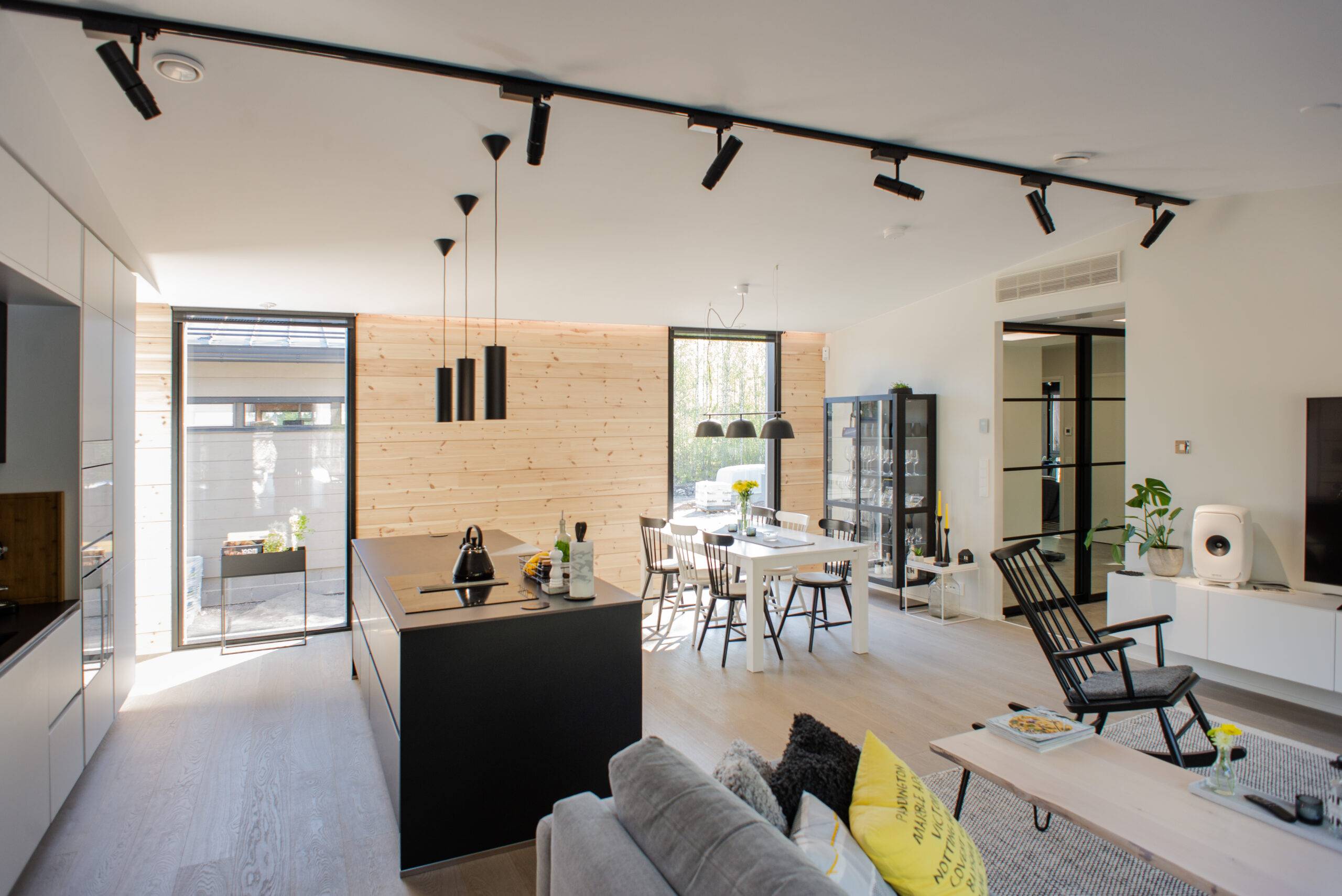 Modernt kök och vardagsrum i öppen planlösning med trädetaljer och svarta möbler för en stilren look. Högkvalitativ interiörbelysning från LedStore.fi skapar en härlig atmosfär och stora fönster släpper in naturligt ljus. 