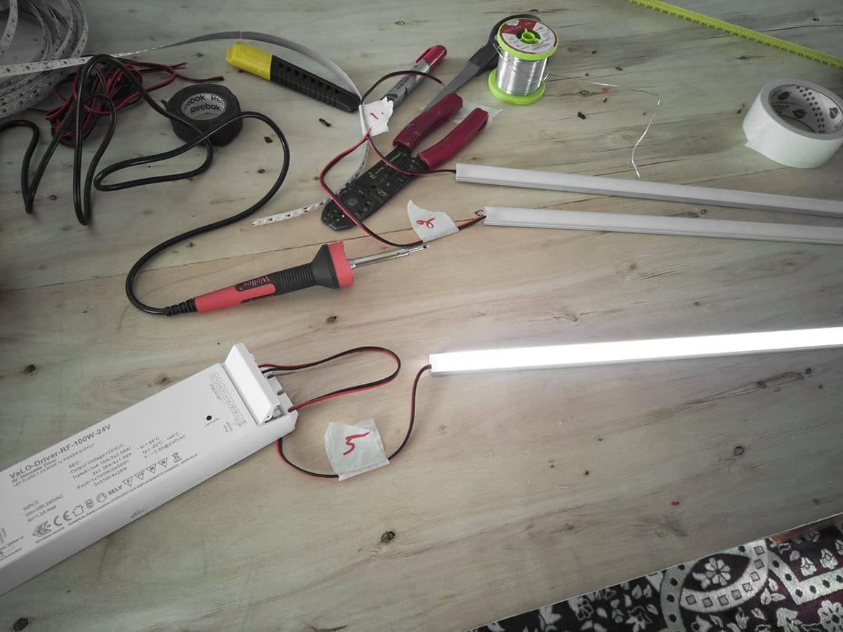 Arbetsbänk med elverktyg, LED-remsor, kablar, lysrör; inkluderar tång, multimeter, lödtråd och strömförsörjning.