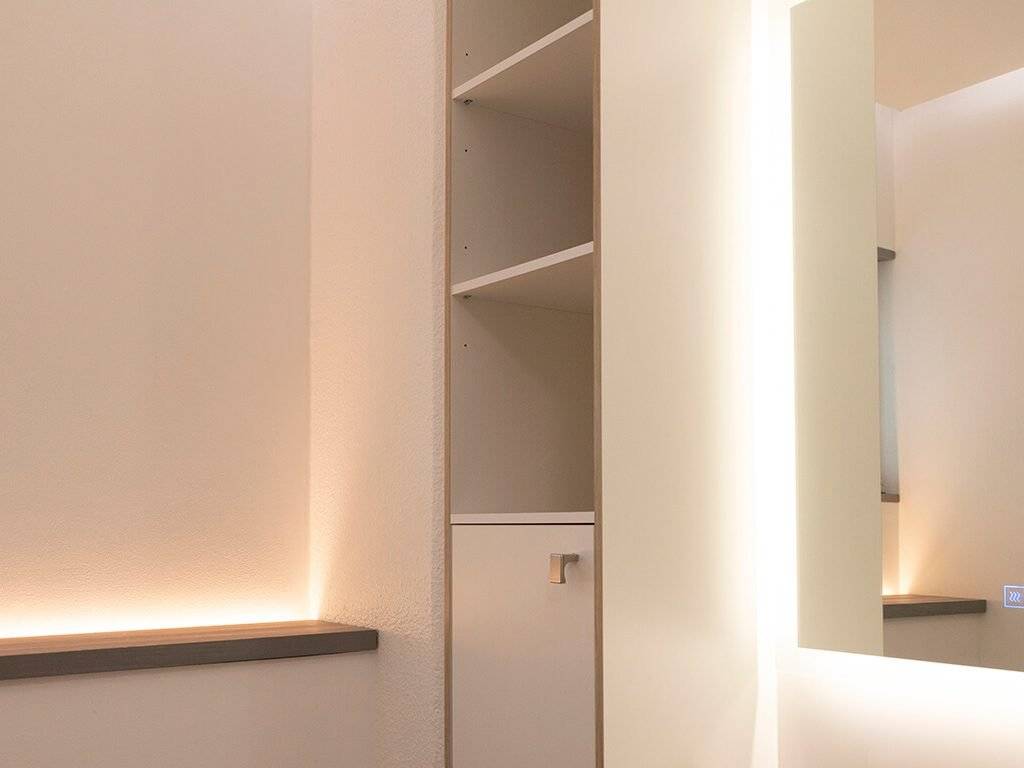 Minimalistisk inredning, moderna hyllor med LED-lampor, spegelvägg, dämpad belysning. Neutrala färger och rena linjer skapar ett elegant och stilfullt utrymme.
