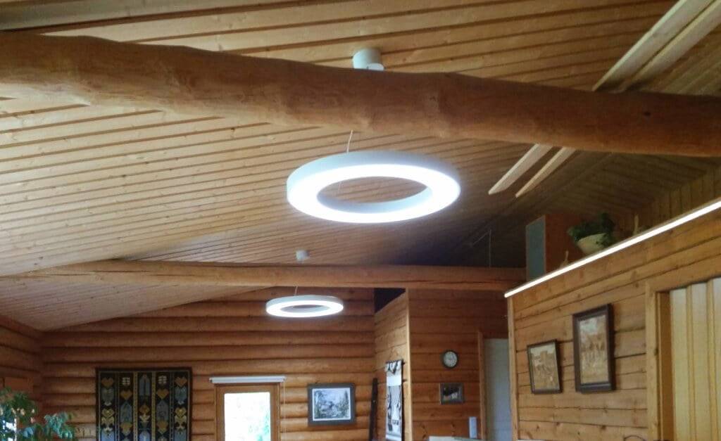 LedStore.fi verkkokaupasta löydät täydelliset led-valaisimet luomaan tunnelmaa rustiikkiseen huoneeseen, jossa på puukatot ja -seinät. Modernt, pyöreät LED-valaisimet tuovat tillaan ajankohtaista tyylikkyyttä. Seiniä koristavat taideteokset ja valokuvat, ja vasemmalla näkyy vehreä kasvi. Kauempana oleva seinä saa lisää ilmettä kauniin seinävaatteen avulla.
