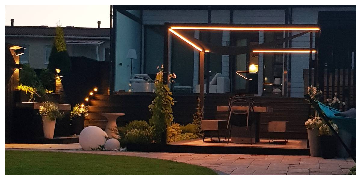 Modern uteplats på bakgården med pergola och fantastisk LED-stämningsbelysning. Trappsteg i trä och stämningsfulla krukväxter. Ensemblen ligger på innergården till ett modernt hus och utgör den perfekta miljön för utekvällar med LedStore.fi:s högkvalitativa LED-belysning.  
