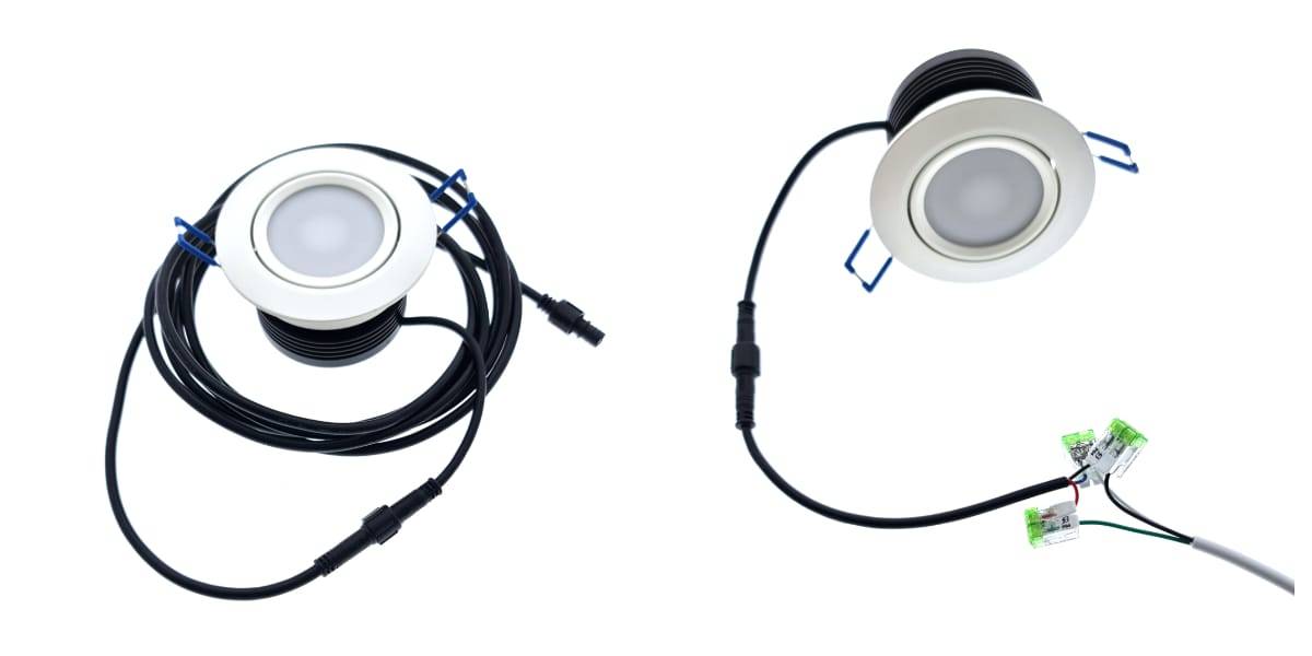 Två runda LED-downlights med vit ram är anslutna till långa svarta ledningar. Lamporna har kontakter i ändarna av ledningarna. Den ena kabeln är tvinnad, medan den andra sträcker sig och ansluts till de gröna inline-kontakterna och markerar sin egen eleganta LED-integration.