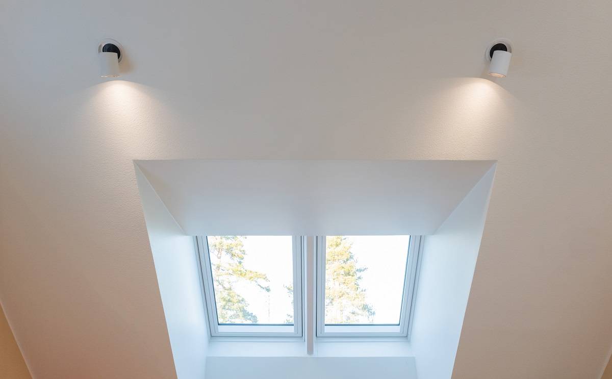 Det vita taket är utrustat med två dubblerade LED-lampor som ger en stark belysning av taklanterninen. Två rektangulära fönster öppnar upp mot taklanterninen och erbjuder utsikt över den blå himlen och trädtopparna. Detta fantastiska belysningsset finns tillgängligt på LedStore.fi, där ett brett utbud av högkvalitativa LED-lampor väntar på dig för att skapa den perfekta atmosfären i ditt hem.