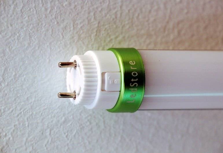 Lähikuva LedStore.fi LED-putkivalaisimesta, metallipäät ja vihreä LedStore-merkintä, taustalla teksturoitu seinä.