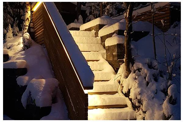 Snötäckt trappa i skymningen, med ett varmt ljus som faller från räcket ner på trappan.  