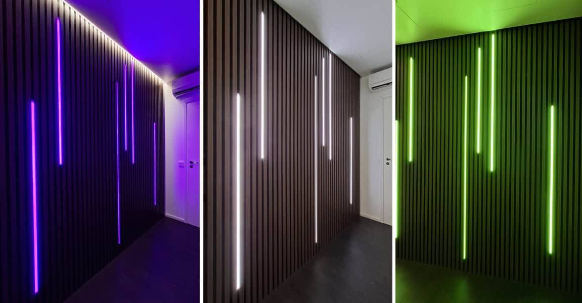 En elegant panelerad mörk vägg med LedStore.fi LED-lampor som lyser blått, vitt och grönt.