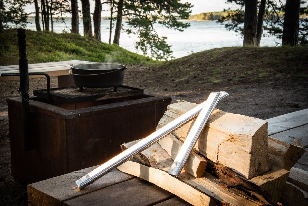 Två WANDA-lampor av olika längd lutade mot trädstammar utomhus.